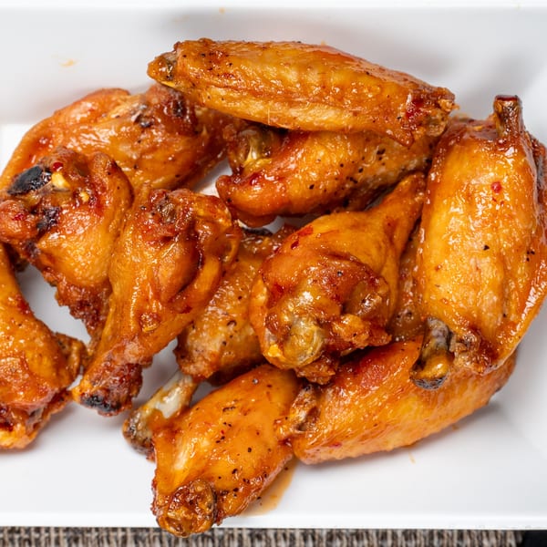 Close-up of a pile of golden-brown, glazed chicken wings in a white dish.