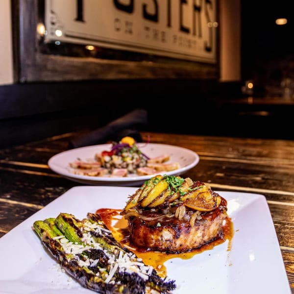 Grilled pork chop with peaches and asparagus, with another dish blurred in the background at Foster's on the Point.