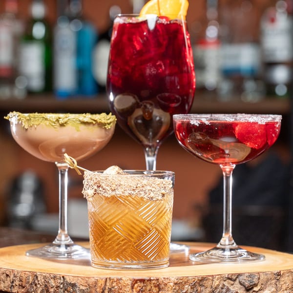 Four colorful cocktails, including a red sangria and a brown martini, on a wooden bar top.