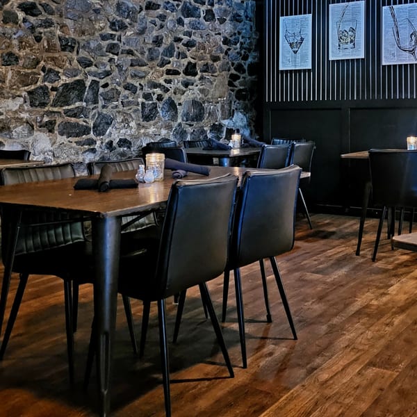 Cozy dining room at Foster's on the Point with dark tables, black chairs, and a stone wall.