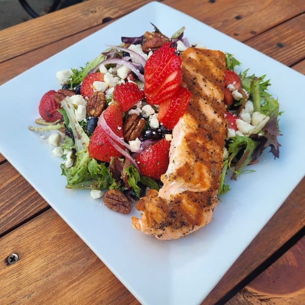 Grilled salmon on a bed of mixed greens with strawberries, pecans, blueberries, red onion, and feta.